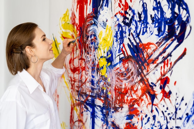 Zdjęcie terapia sztuką zabawa wypoczynek kreatywne hobby szczęśliwy inspirowany uśmiechający się leworęczny artysta kobieta cieszący się malowaniem kolorowy żółty niebieski czerwony rozmazany odcisk dłoni abstrakcyjna grafika na białej ścianie