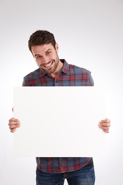 Teraz to, o czym mówię, zdjęcie studyjne uśmiechniętego młodego mężczyzny trzymającego pusty biały plakat