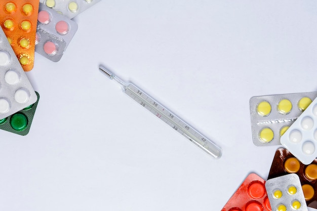 Termometr na białym tle wśród tabletek w różnych kolorach w opakowaniach
