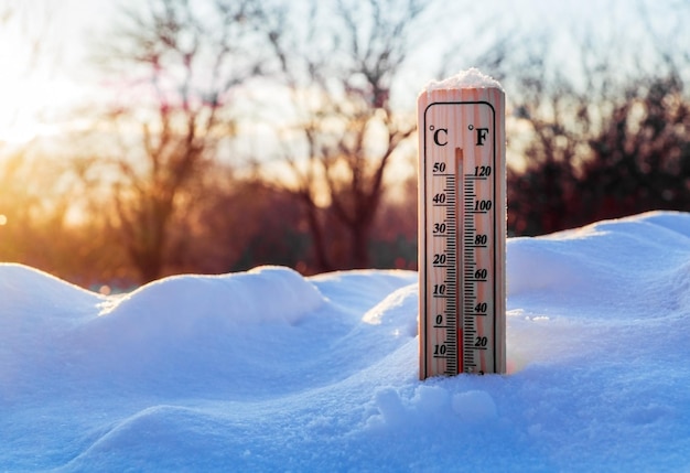 Termometr na śniegu pokazuje zerową temperaturę przed wiosną na tle zachodu słońca