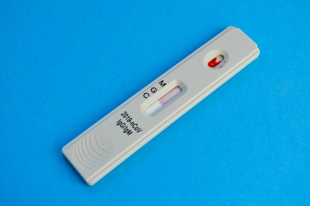 Test na koronawirusa leży na niebieskim tle kropli krwi żylnej na ekspresowym pasku testowym