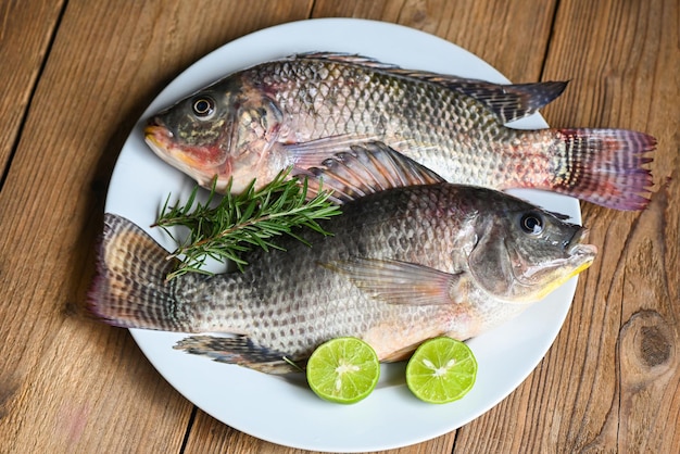 Tilapia z białym talerzem z rozmarynową cytryną limonką na drewnianym tle Świeże surowe ryby tilapia z farmy tilapia