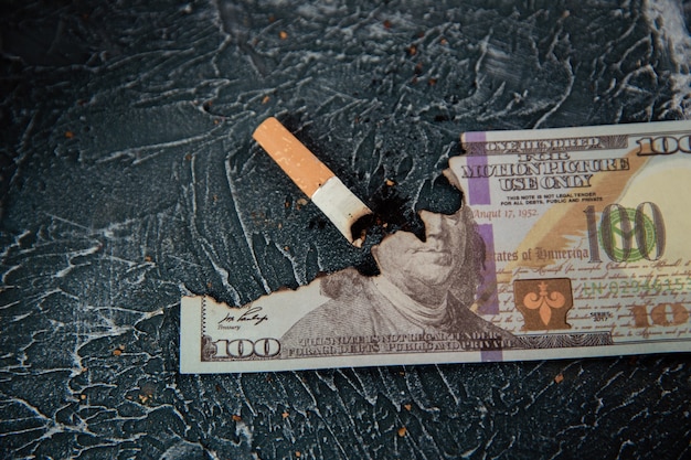 Tlący się papieros i dolar na szarym stole