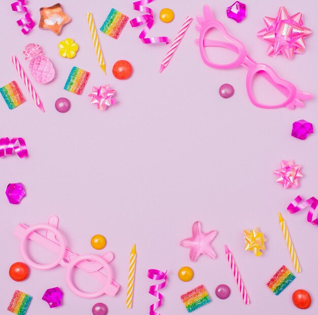 Tło urodzinowe dla dzieci ze świeczkami, słodyczami i atrybutami partii na fioletowej powierzchni