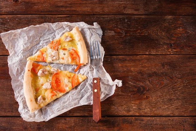 Tło włoskiej tradycyjnej żywności. Dwa kawałki pysznej pizzy podane na białej papierowej serwetce, na drewnianym stole w stylu rustykalnym, leżące na płasko. Ciemne tło z wolnym miejscem na tekst.