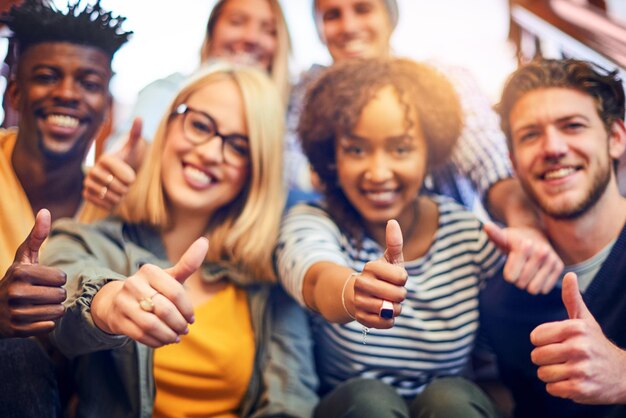 To aprobata dla szkolnictwa wyższego Portret grupy różnorodnych studentów pokazujących kciuk w górę, siedząc na schodach w kampusie