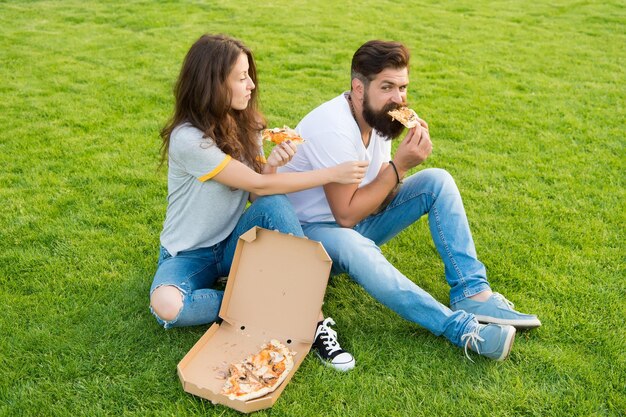 To jest mój kawałek letni piknik na zielonej trawie szczęśliwa para je pizzę rodzinny weekend para zakochana randka fast food brodaty mężczyzna hipster i urocza dziewczyna jedzą pizzę
