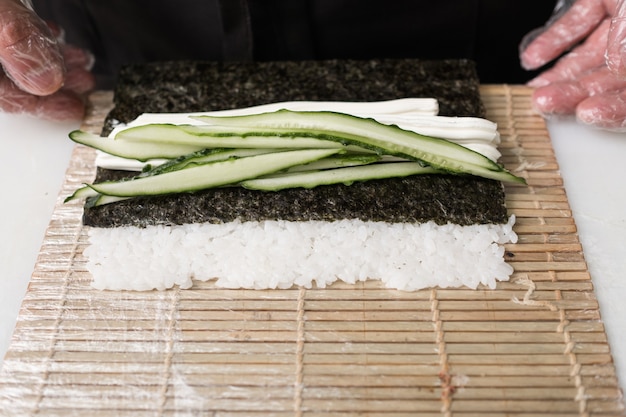 To jest smaczne. Szef kuchni przygotowuje sushi tocząc ogórki w ryżu i nori. Koncepcja świeżych składników