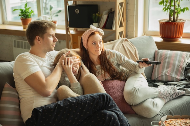 To nie dla dzieci. Rodzina spędzająca miło czas razem w domu. Wygląda na zdziwionego. Mama, tata i córka bawią się, jedzą pizzę, oglądają telewizję. Razem, domowy komfort, miłość, koncepcja relacji.