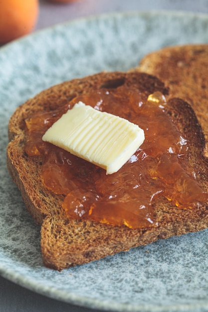 Zdjęcie toast z masłem i dżemem z morelkami na szarym talerzu na szarem tle