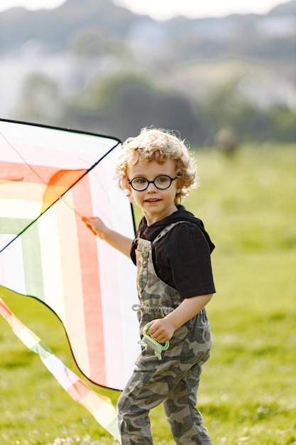 Zdjęcie toddler chłopiec bawi się latawcem w parku. chłopiec ubrany w kombinezon w kolorze khaki. mały chłopiec biegający po trawie z latawcem