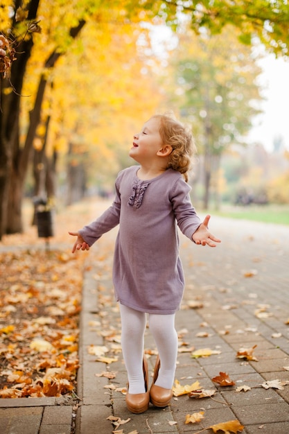 toddler girl with curly hair in a purple knitted dress walking in an autumn park wearing her mom large beige high heels