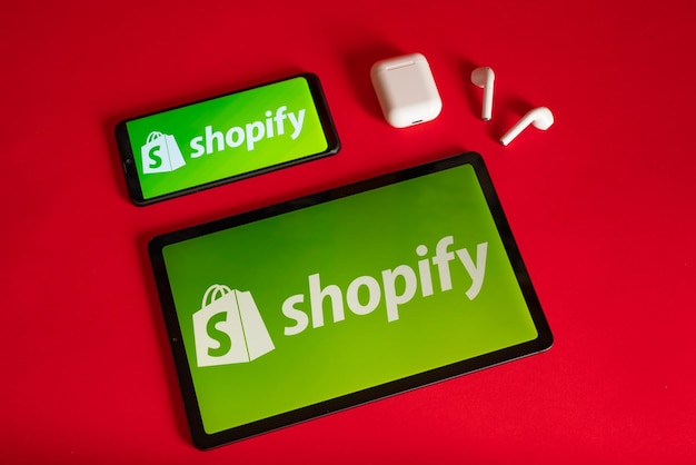 Tokio Japonia 05 czerwca 2022 Strona internetowa Shopify wyświetlana na nowoczesnym laptopie, smartfonie i notebooku na czerwonym tle Logo Shopify na iPhonie