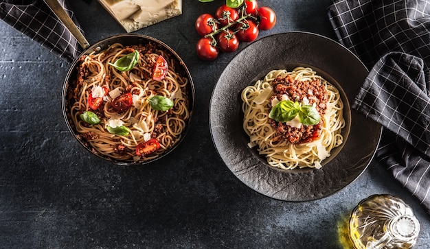 Top of view włoski makaron spaghetti bolognese na talerzu i patelni z pomidorami i bazylią.