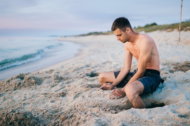 Topless mężczyzna na plaży tworząc formy piasku.