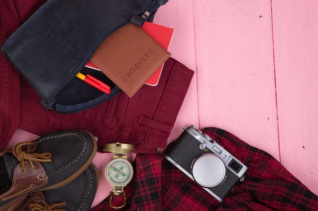 Torba na rzeczy turystyczne paszport aparat kompas buty koszula notatnik na różowym drewnianym tle