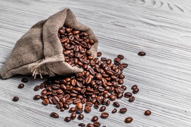 Torebka z naturalnych brązowych ziaren kawy i niektórych rozrzuconych nasion jasnego drewna. Ziarna kawy palonej rozlewają worek na stół.
