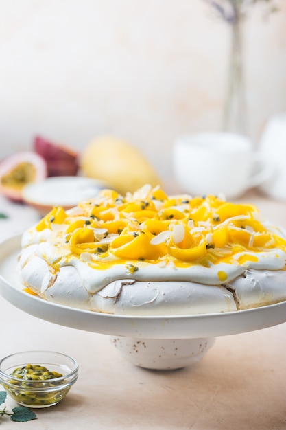 Tort bezowy Pavlova ze świeżym mango i marakui oraz bitą śmietaną na tle łupkowym, kamiennym lub betonowym