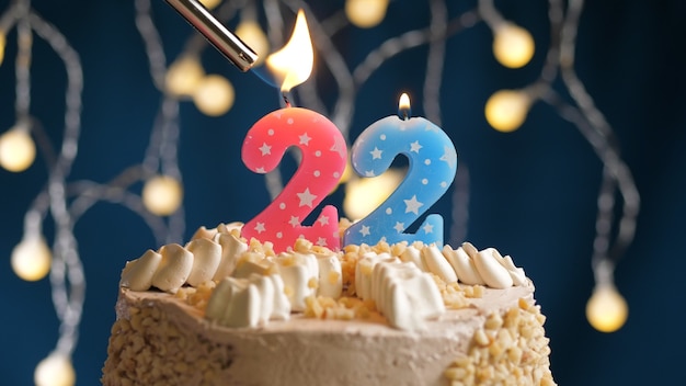 Zdjęcie tort urodzinowy z 22 numerami różowej świecy na niebieskim tle podpalony przez zapalniczkę. zamknąć widok