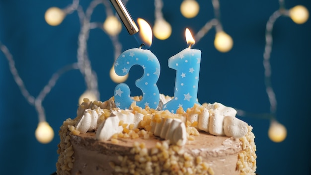 Tort urodzinowy z 31 numerami świec na niebieskim tle podpalony przez zapalniczkę. Zbliżenie