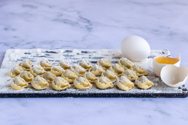 Tortellini posypane mąką na ciemnej desce na marmurze