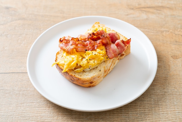 tost chlebowy z jajecznicą i bekonem na białym talerzu