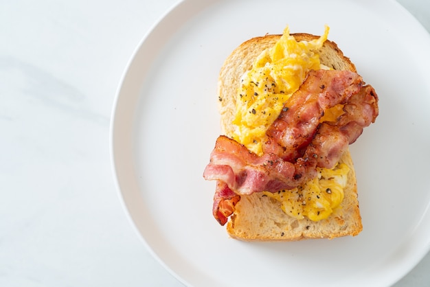 tost chlebowy z jajecznicą i bekonem na białym talerzu