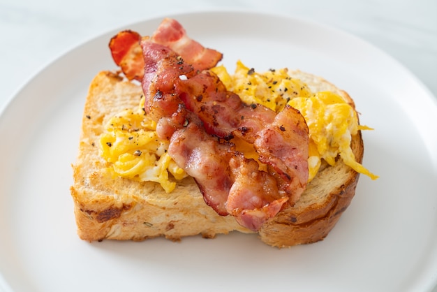 tost chlebowy z jajecznicą i bekonem na białym talerzu