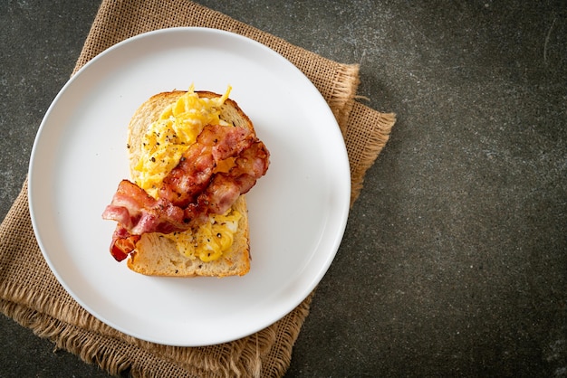 tost chlebowy z jajecznicą i bekonem na białym talerzu