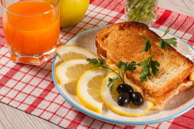 Tost z masłem i plasterkami sera z cytryny i oliwkami na talerzu jabłkowym i szklanką soku pomarańczowego