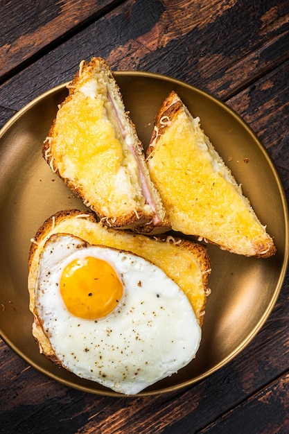 Tosty Francuskie Croque Monsieur I Croque Madame, Grillowane Kanapki Na Bułce Briochowej Z Plastrowaną Szynką, Roztopionym Serem Emmentaler I Jajkiem. Drewniane Tło. Widok Z Góry.