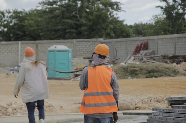 Trabajadores Con Trajes De Proteccion En Construccion Llevan Grupo De Barillas De Acero En Conjunto, Vista Trasera