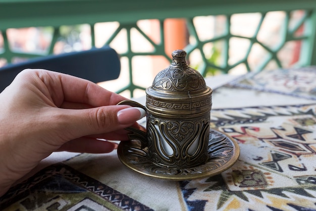 Tradycyjna kawa po turecku. Orientalna kawa na stole w miedzianej filiżance. Kobieca ręka trzyma kubek. Tbilisi, Gruzja. Zdjęcie wysokiej jakości
