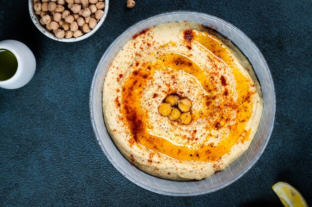 Tradycyjna przystawka z Bliskiego Wschodu Hummus podawana z cytryną i tahini, doprawiona oliwą extra vergine i papryką w ceramicznym talerzu. danie wschodnie. Danie wegetariańskie. Tradycyjny dip z ciecierzycą.