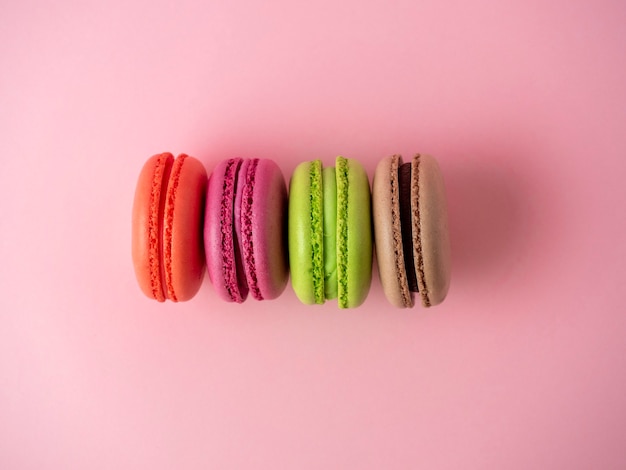 Tradycyjne ciasteczka makaroniki w różnych kolorach leżą na różowym tle.