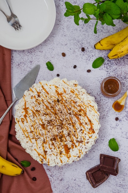 Tradycyjne ciasto Banoffee ze świeżymi bananami, bitą śmietaną, czekoladą, kawą i toffi. Bez deseru do pieczenia. Orientacja pionowa. Widok z góry.