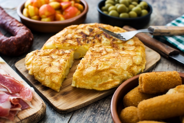 Tradycyjne hiszpańskie tapas. Krokiety, oliwki, omlet, szynka i patatas bravas na drewnianym stole