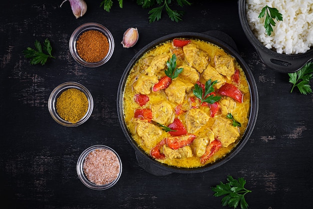 Tradycyjne indyjskie curry masala z kurczaka. Indyjskie curry z kurczaka ze słodką papryką i ryżem w misce, przyprawy, ciemne tło. Tradycyjne danie indyjskie. Widok z góry, układ płaski