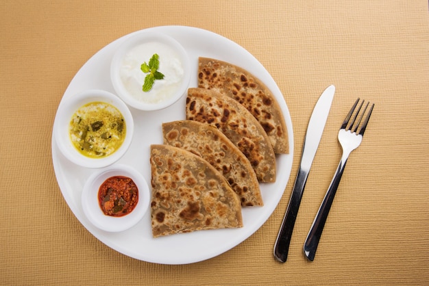 Tradycyjne indyjskie jedzenie Aloo paratha lub płaski chleb nadziewany ziemniakami. podawane z ketchupem i twarogiem na kolorowym lub drewnianym tle. Selektywne skupienie