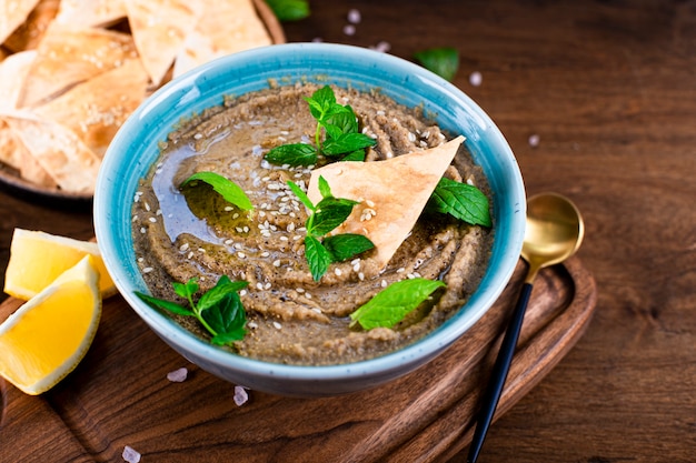 Tradycyjne Orientalne Przekąska Baba Ganoush Z Sezamem I Liśćmi Mięty Z Bliska. Hummus Z Bakłażana Z Chipsami Pita Na Drewnianym Stole.