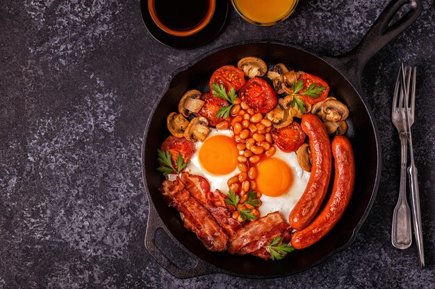 Tradycyjne pełne śniadanie angielskie ze smażonymi jajkami, kiełbasą, fasolą, pieczarkami, grillowanymi pomidorami i boczkiem.