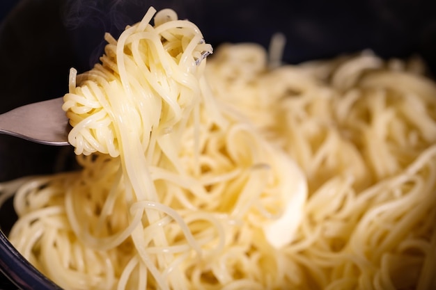 Zdjęcie tradycyjne spaghetti kompozycja spożywcza z gorącym makaronem w patelni i kawałkiem masła na czarnym tle śródziemnomorskie potrawy włoskie proste danie