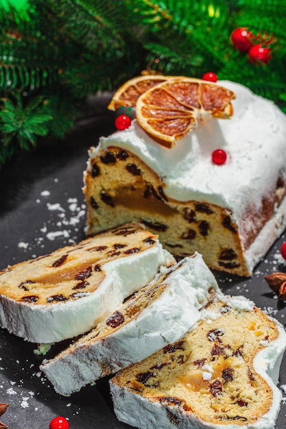 Tradycyjne świąteczne ciasto niemieckie ciasto europejskie pachnące domowe pieczywo z przyprawami i suszonymi owocami gałęzie choinki i dekoracje czarne tło z bliska
