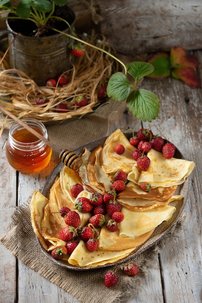 Zdjęcie tradycyjne ukraińskie lub rosyjskie naleśniki z jagodami truskawek i miodem na drewnianym stole