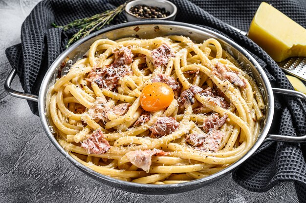 Tradycyjne włoskie danie spaghetti carbonara z boczkiem w sosie śmietanowym na patelni. Szare tło. Widok z góry