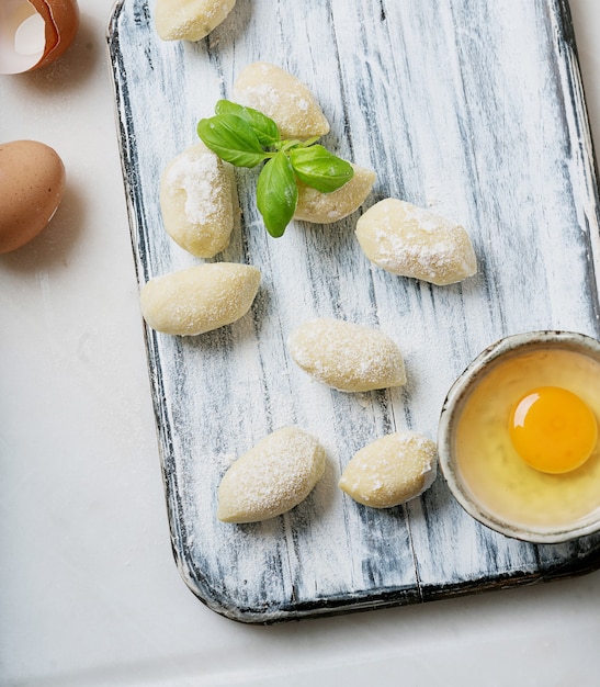 Tradycyjne włoskie gnocci ziemniaczane (makaron) ozdobione listkiem bazylii, jajkami, mąką. Koncepcja niegotowanego makaronu. Widok z góry. Flat Lay