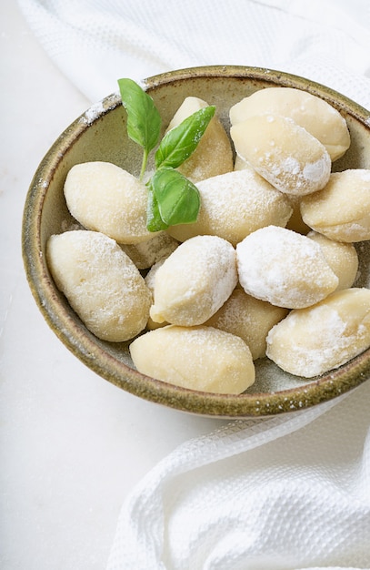 Tradycyjne włoskie gnocci ziemniaczane (makaron) ozdobione listkiem bazylii, jajkami, mąką. Koncepcja niegotowanego makaronu.