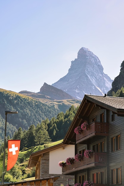 Tradycyjny domek w Zermatt ze szczytem Matterhorn ze szwajcarską flagą, Szwajcaria latem.