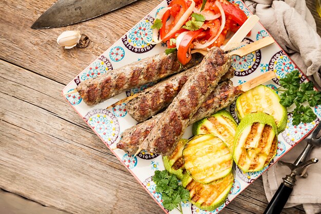 Zdjęcie tradycyjny domowy grillowany turecki kebab adana urfa, kebab z mięsa mielonego, na talerzu z sałatką pomidorową i cukinią na drewnianym