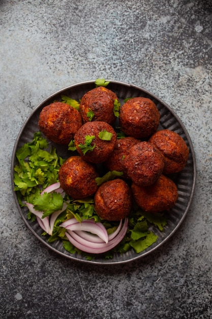 Tradycyjny falafel z Bliskiego Wschodu podawany ze świeżą zieloną kolendrą i sałatką z cebuli. Arabski lub śródziemnomorski falafel przystawka podawany na rustykalnym tle stołu. Widok z góry